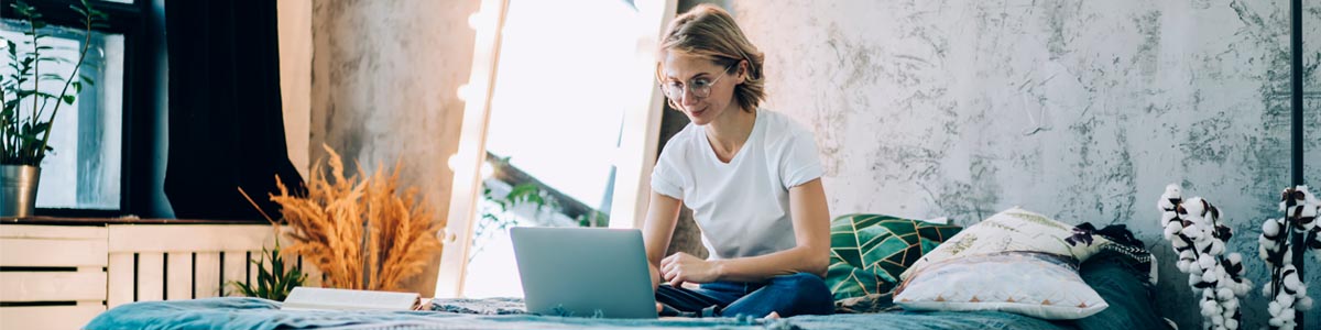 Young woman looking at laptop computer while sitting on bed