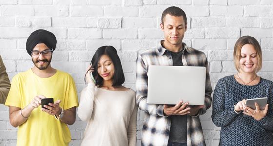 Group of people looking at different devices including laptops and mobile phones