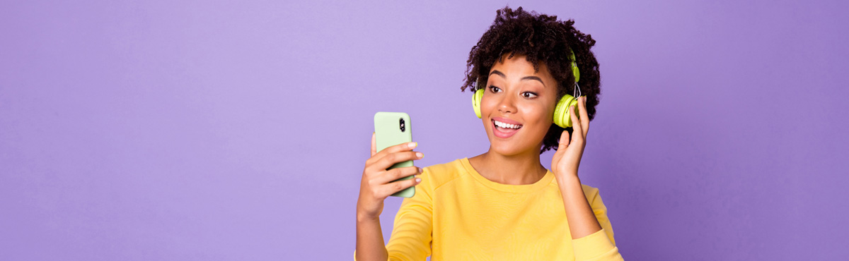 Young woman with headphones on looking at phone on purple background