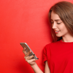 Young woman looking at phone in front of red background