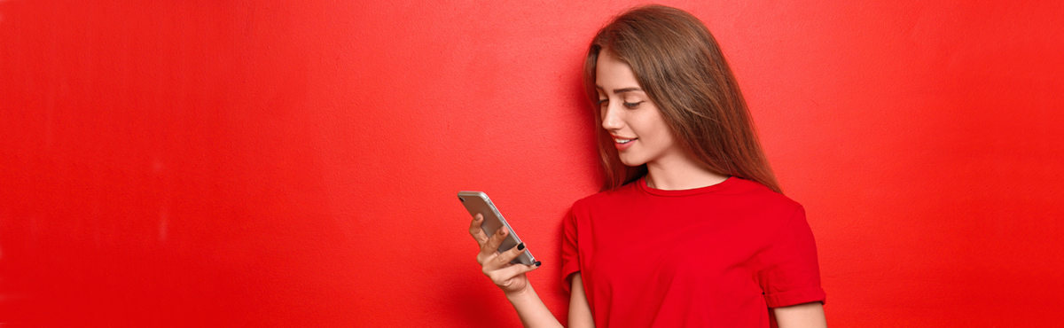 Young woman looking at phone in front of red background