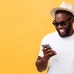 Young man wearing hat holding phone infront of a yellow background