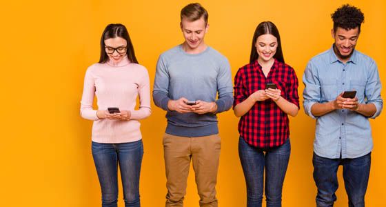 Four people holding and looking at mobile phones against yellow background