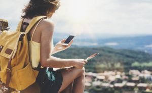 Hipster young girl with bright backpack looking at phone and map