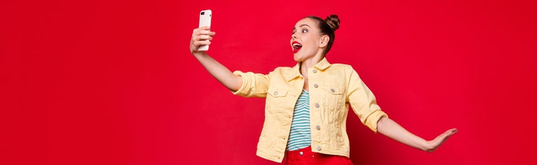 Young excited woman looking at phone against red background