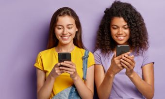 Two young women looking at phones against purple background