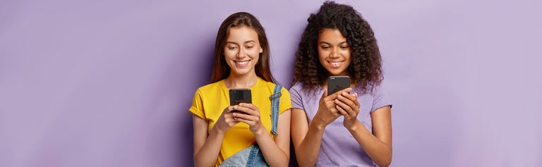 Two young women looking at phones against purple background