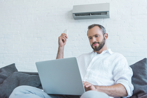 Man with laptop turning on air conditioner at home on lounge