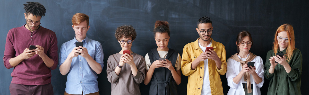 Group of people standing against dark wall looking at smartphones