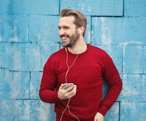 Man listening to music on phone against blue wall