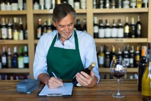 Small business owner at desk of wine shop looking at bottle