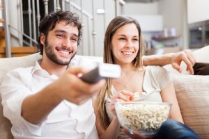 Young couple on couch watching tv with remote and popcorn