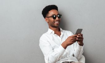 Young man wearing sunglasses looking at mobile phone against grey background