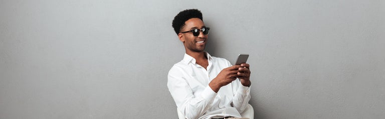 Young man wearing sunglasses looking at mobile phone against grey background