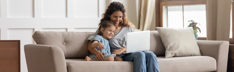 Woman and daughter on sofa looking at laptop computer in the home