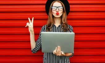 Happy young woman holding laptop in front of red wall