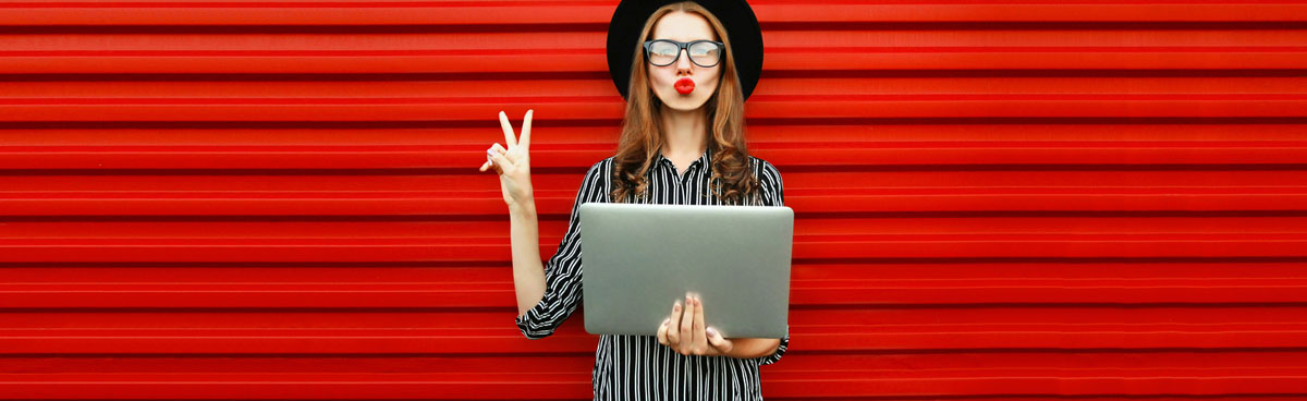 Happy young woman holding laptop in front of red wall