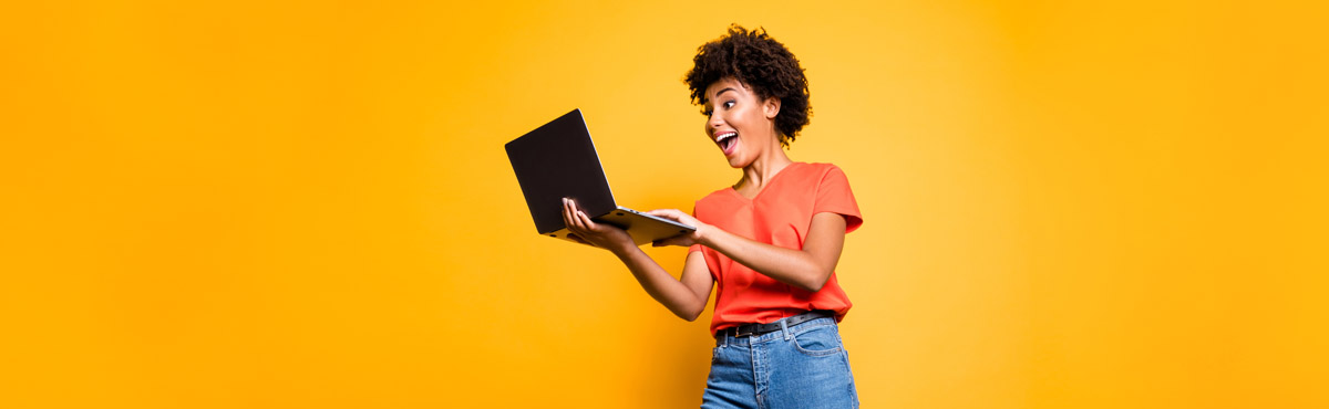 Young woman looking excitedly at computer against yellow background