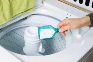 person putting laundry powder in a top loader washing machine