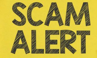 Scam alert warning text on yellow background and wood table