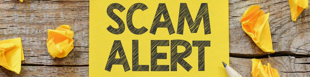 Scam alert warning text on yellow background and wood table