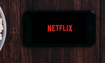 Flat shot of phone with Netflix logo next to popcorn and white headphones