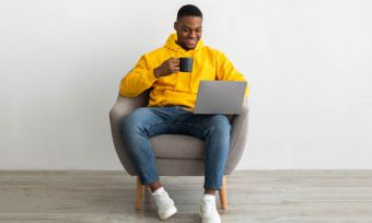 Young man in yellow hoodie using laptop while sitting in chair