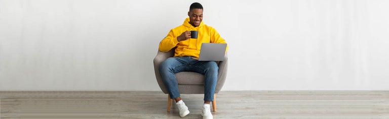 Young man in yellow hoodie using laptop while sitting in chair