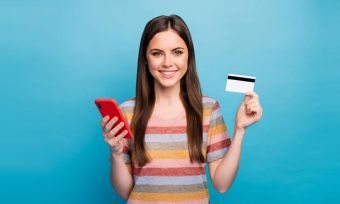 Young woman holding phone and bank card against blue background