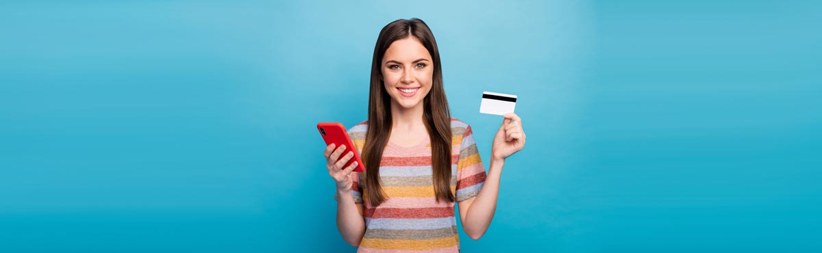 Young woman holding phone and bank card against blue background