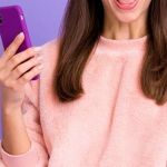 A woman using a phone in front of a purple background