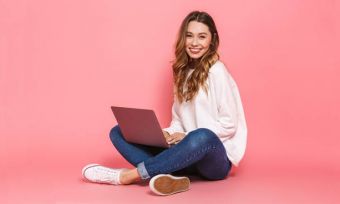 Woman using laptop against pink backdrop