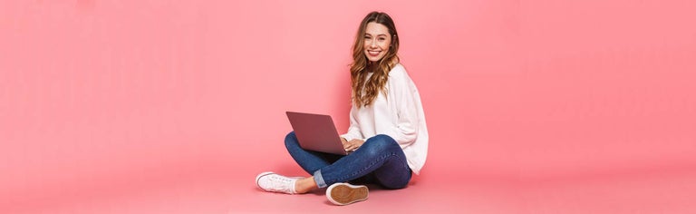 Woman using laptop against pink backdrop