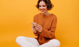 Young woman using phone in front of yellow backdrop