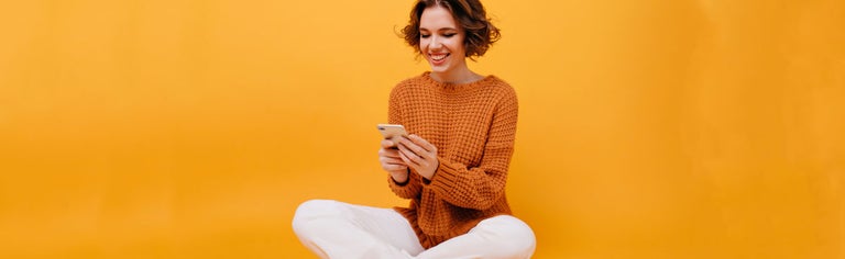 Young woman using phone in front of yellow backdrop