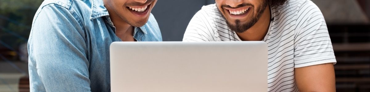 Two mates smiling and using a laptop together