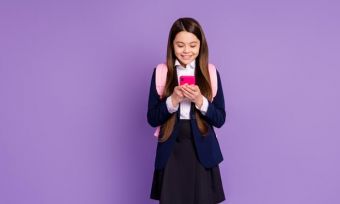 Girl wearing school uniform with backpack on looking at mobile phone