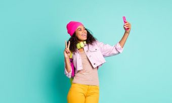 Young woman holding phone taking selfie against teal background