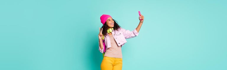 Young woman holding phone taking selfie against teal background