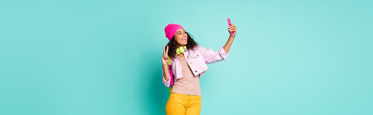 Young woman holding phone taking selfie against teal background