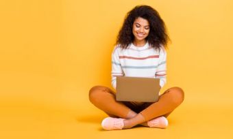 Young woman looking at laptop against yellow background