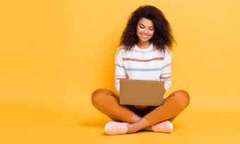 Young woman looking at laptop against yellow background