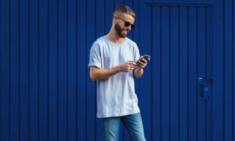 Young man using smartphone while leaning against blue wall