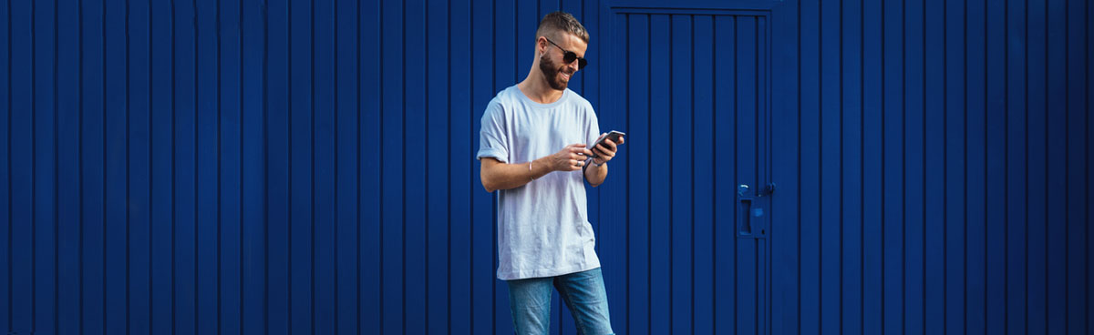 Young man using smartphone while leaning against blue wall