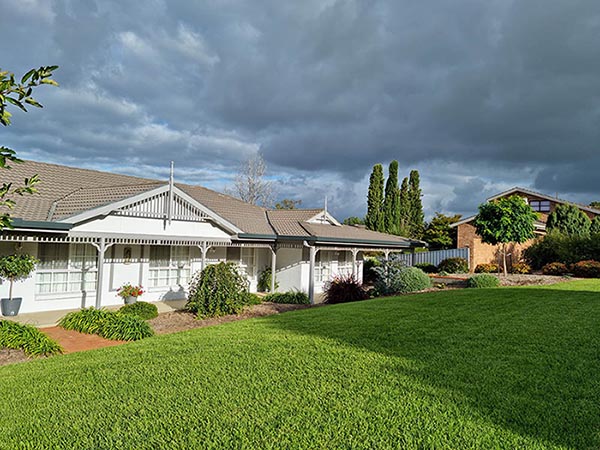 A grey house with a green lawn and dark storm clouds.