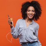Young woman holding phone against orange background