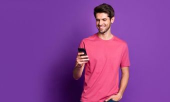 Young man looking at mobile phone against purple background