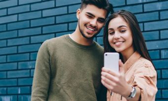 Young couple taking selfie in front of blue brick wall