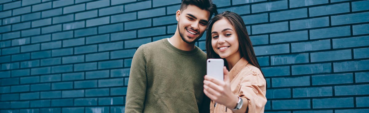 Young couple taking selfie in front of blue brick wall