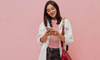 Young woman using smartphone against pink background